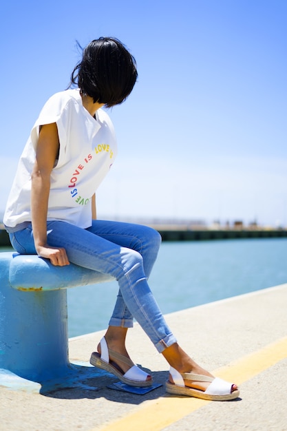 Menina com roupas casuais sentada no porto no verão