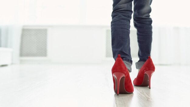 Menina com sapatos vermelhos de mãe está andando pela casa. Vista traseira, copyspace