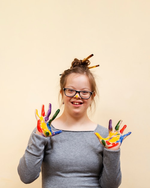 Foto menina com síndrome de down posando ao mostrar as palmas das mãos coloridas
