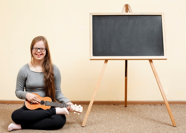 Menina com síndrome de down posando com guitarra e quadro-negro