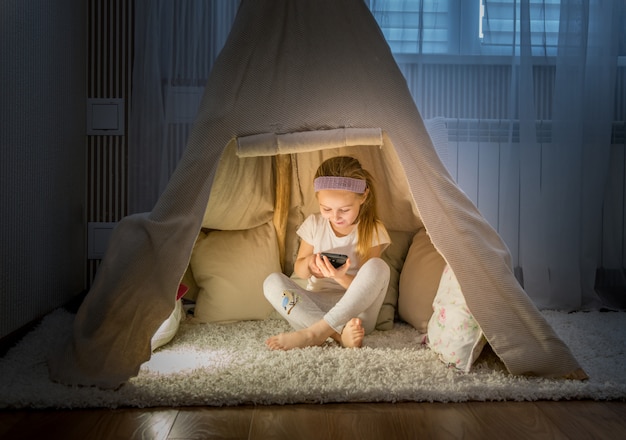 Menina com smartphone sentado na tenda