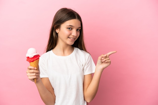 Menina com sorvete de corneta sobre fundo rosa isolado apontando o dedo para o lado