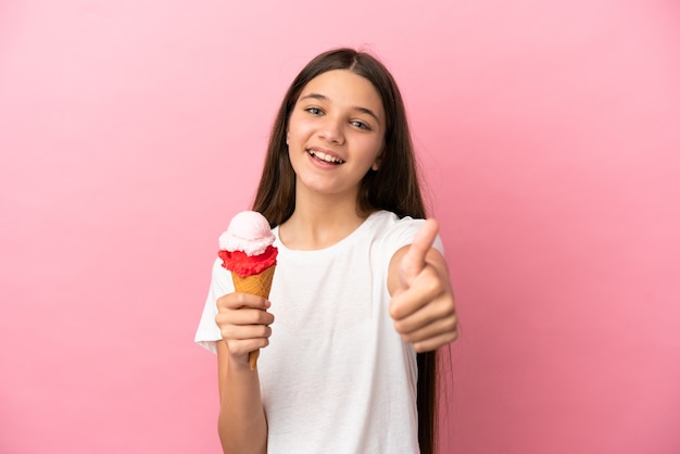 Menina com sorvete de corneta sobre fundo rosa isolado com polegar para cima porque algo bom aconteceu