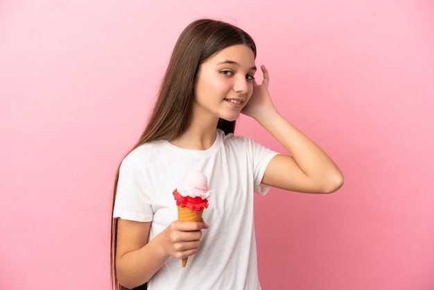 Menina com sorvete de corneta sobre fundo rosa isolado ouvindo algo colocando a mão na orelha