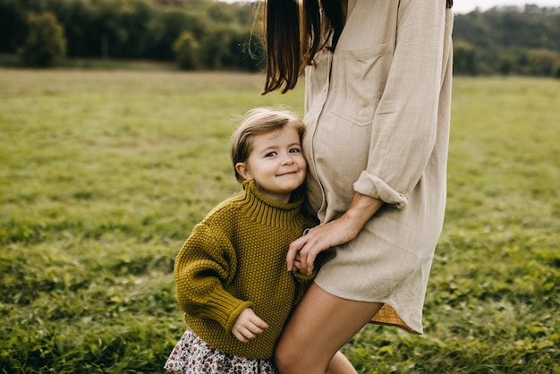 Foto menina com sua mãe grávida ao ar livre ouvindo o que está acontecendo dentro da barriga