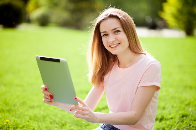 Menina com tablet sentada no gramado e sorrindo