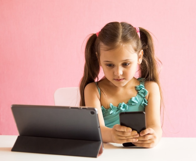 Menina com telefone e tablet na mesa