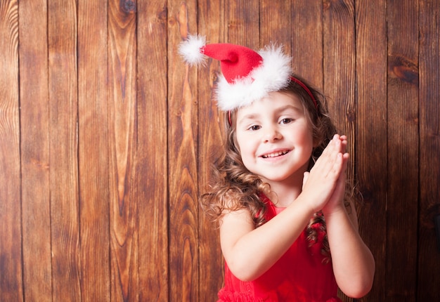 Menina com tiara de chapéu de Papai Noel sentada na parede de madeira, copie o espaço