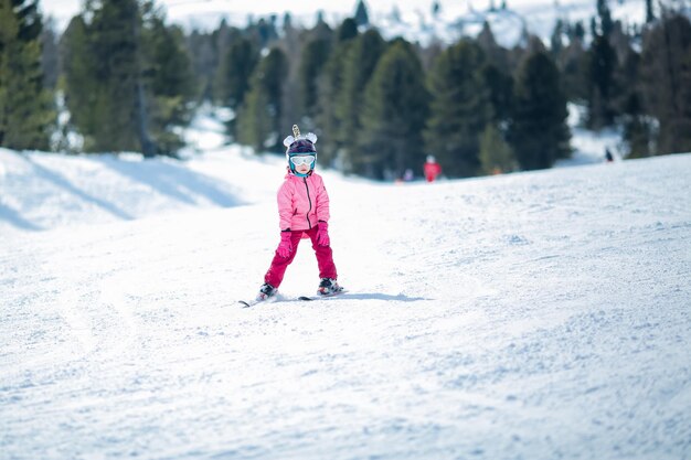 Menina com traje de esqui rosa esquiando em declive Atividade recreativa esportiva de inverno