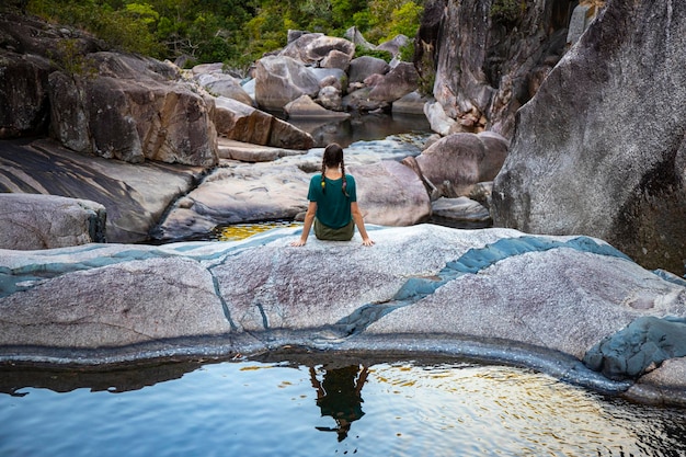 menina com tranças senta-se em rochas coloridas em jourama cai ao pôr do sol, queensland, austrália