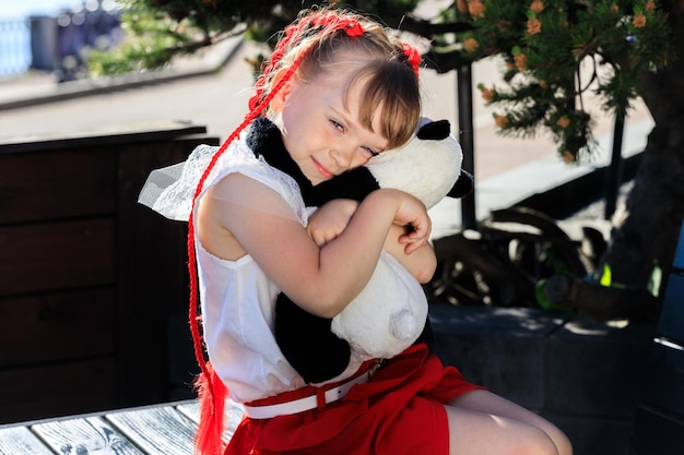 Menina com tranças vermelhas no parque no verão com um urso de brinquedo panda