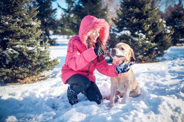 Menina com um cachorro Labrador cachorro brincando no inverno, diversão ao ar livre