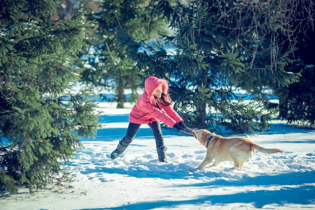 Menina com um cachorro labrador cachorro brincando no inverno, diversão ao ar livre