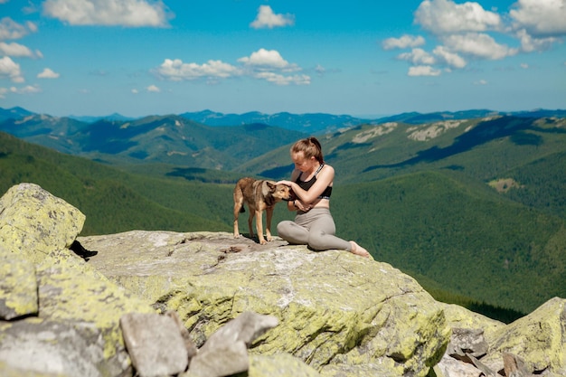 Menina com um cachorro no topo de uma montanha, assistindo a uma bela paisagem com os braços bem abertos