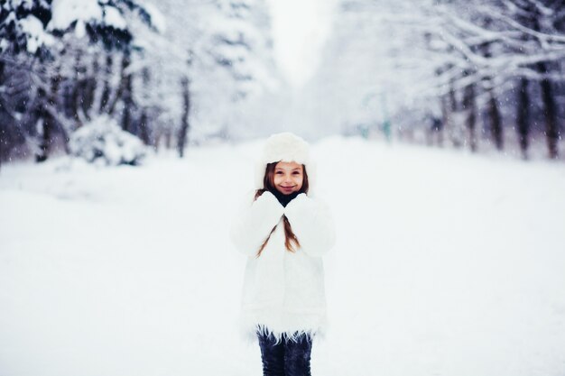 Menina com um casaco de pele em pé em uma floresta de inverno e sorrindo