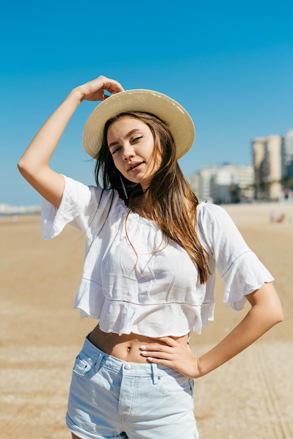 Menina com um chapéu cobrindo os olhos está na praia em uma bela pose