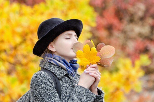 Menina com um chapéu com um buquê de folhas de outono.