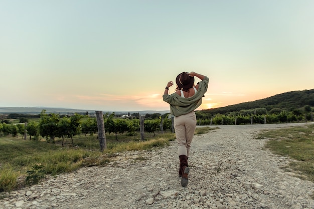 Menina com um chapéu de cowboy ao pôr do sol na zona rural das vinhas.