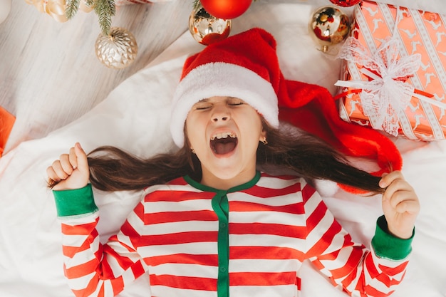 Menina com um chapéu de Papai Noel encontra-se perto da árvore de Natal em casa. vista de cima. Natal.