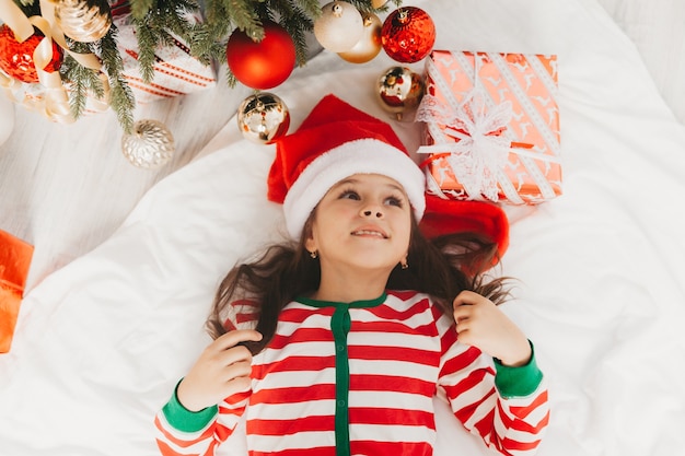 Menina com um chapéu de Papai Noel encontra-se perto da árvore de Natal em casa. vista de cima. Natal.