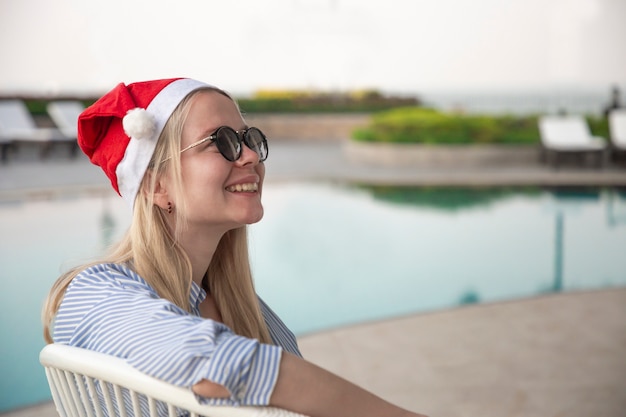 Menina com um chapéu vermelho de natal ao lado da piscina.