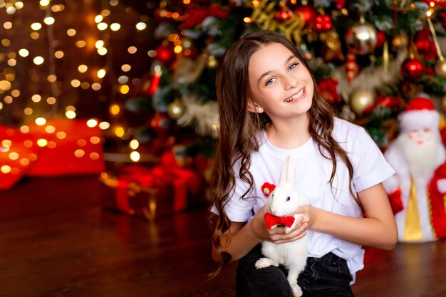 Menina com um coelho branco no fundo de guirlandas de luzes na árvore de natal