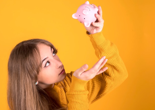 Menina com um cofrinho, não tem dinheiro está olhando para o cofrinho vazio