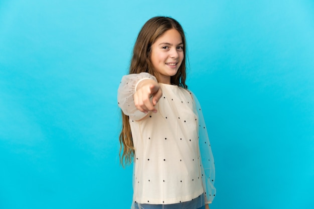 Menina com um fundo azul isolado apontando para a frente com uma expressão feliz