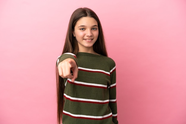 Menina com um fundo rosa isolado apontando para a frente com uma expressão feliz