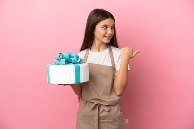 Menina com um grande bolo sobre fundo rosa isolado apontando para o lado para apresentar um produto