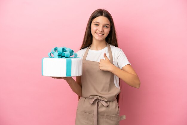 Menina com um grande bolo sobre um fundo rosa isolado fazendo um gesto de polegar para cima