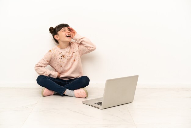 Menina com um laptop sentada no chão sorrindo muito