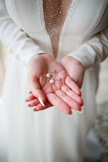 Menina com um lindo vestido branco segurando brincos nas mãos