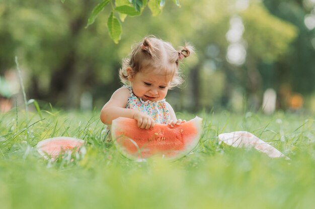 menina com um penteado engraçado come uma melancia no gramado no parque lanche saudável para crianças