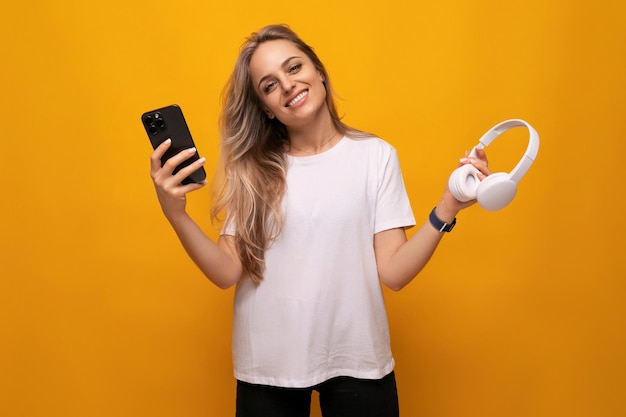 Menina com um smartphone e fones de ouvido nas mãos em um fundo amarelo