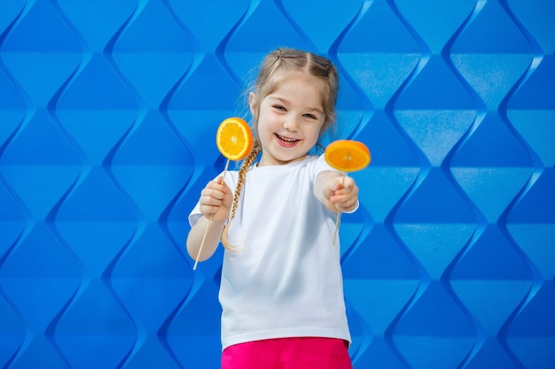 Menina com um sorriso e rabo de cavalo, vestida com uma camiseta branca, segurando meia laranja na mão, conceito de um estilo de vida saudável