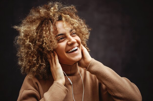 Menina com um sorriso no rosto, segurando as orelhas com as mãos e curtindo música