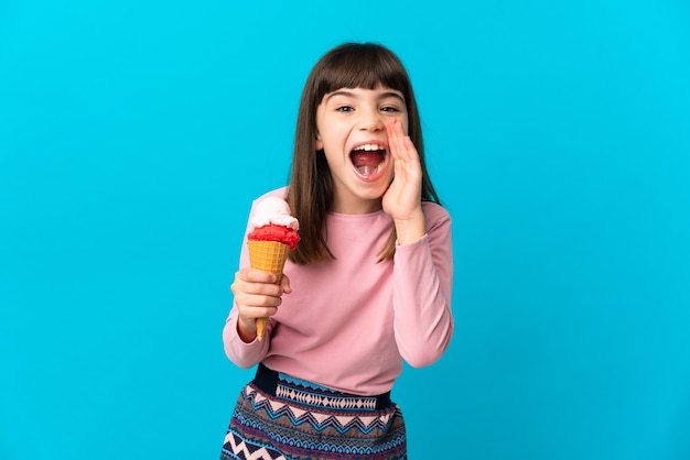 Menina com um sorvete de corneta isolado na parede azul gritando com a boca bem aberta