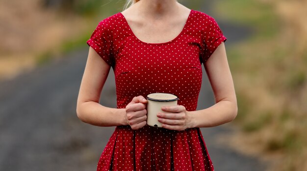 Menina com um vestido de bolinhas com copo na estrada rural