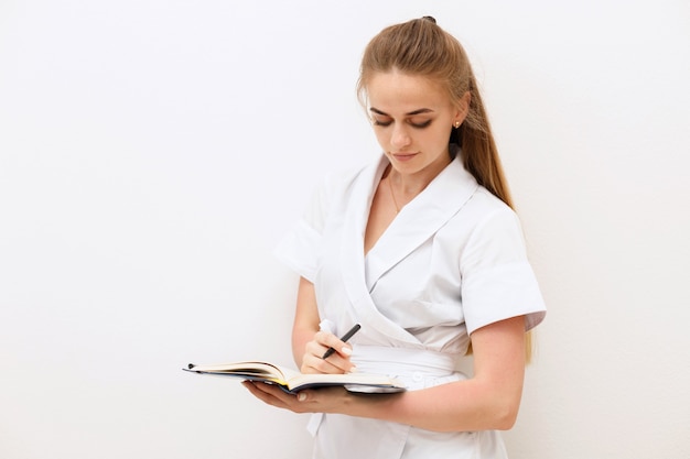 Menina com um vestido de médico com um caderno nas mãos em um fundo branco