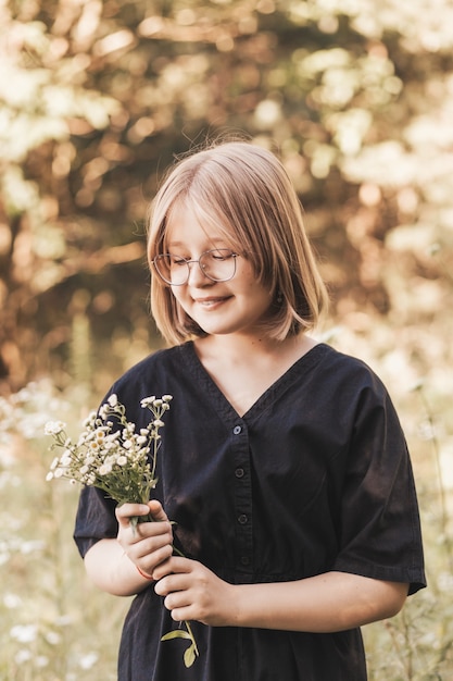 Menina com um vestido preto elegante na natureza no verão com flores