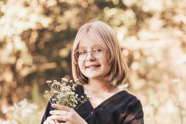 Menina com um vestido preto elegante na natureza no verão com flores