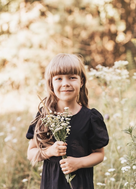 Menina com um vestido preto elegante na natureza no verão com flores