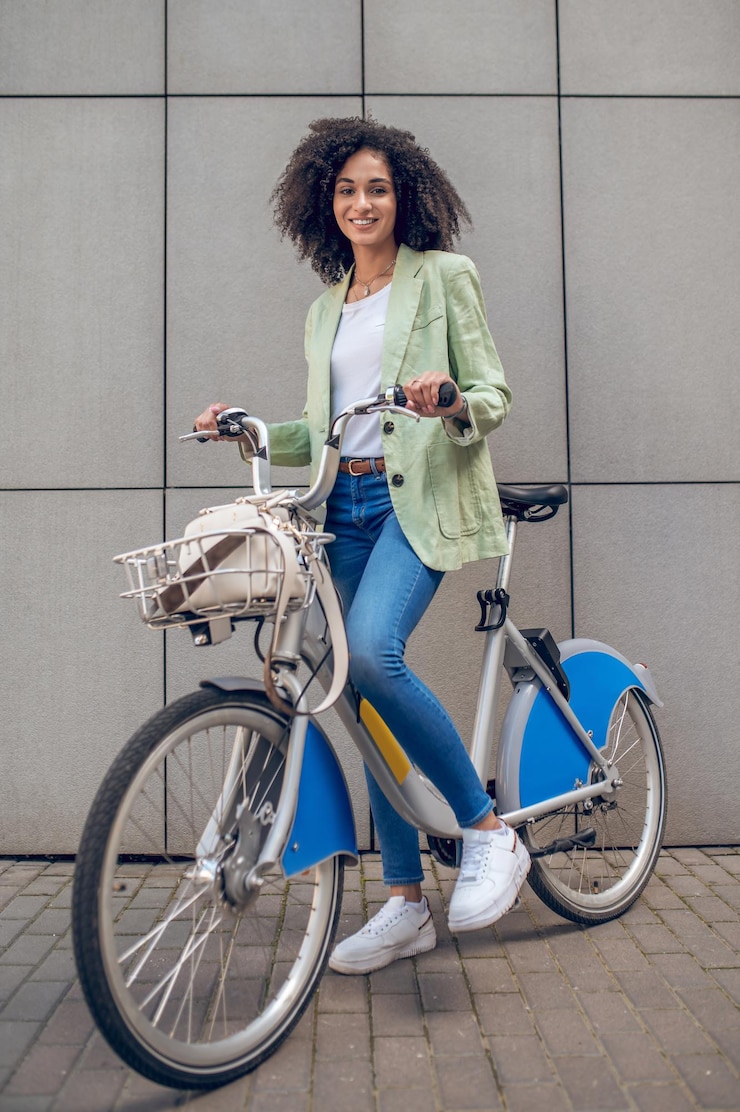 Foto menina com uma bicicleta. menina de cabelos cacheados em roupas da moda com uma bicicleta