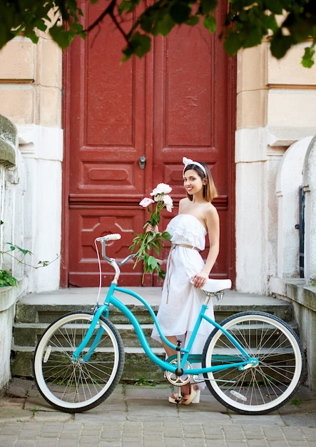 Menina com uma bicicleta retrô e um buquê de peônias