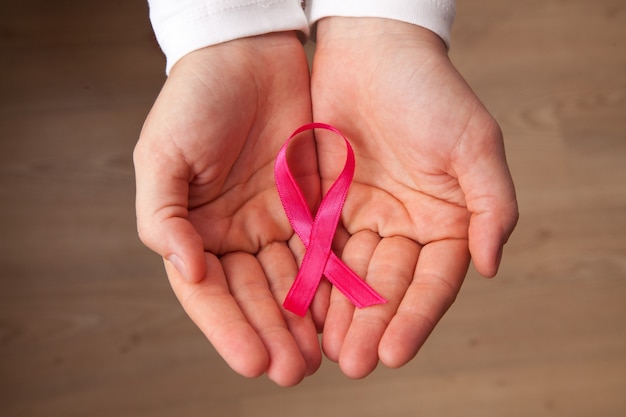 Menina com uma camisa branca com uma fita rosa nas mãos em frente à janela Mês de conscientização do câncer de mama Conceito de câncer de mama