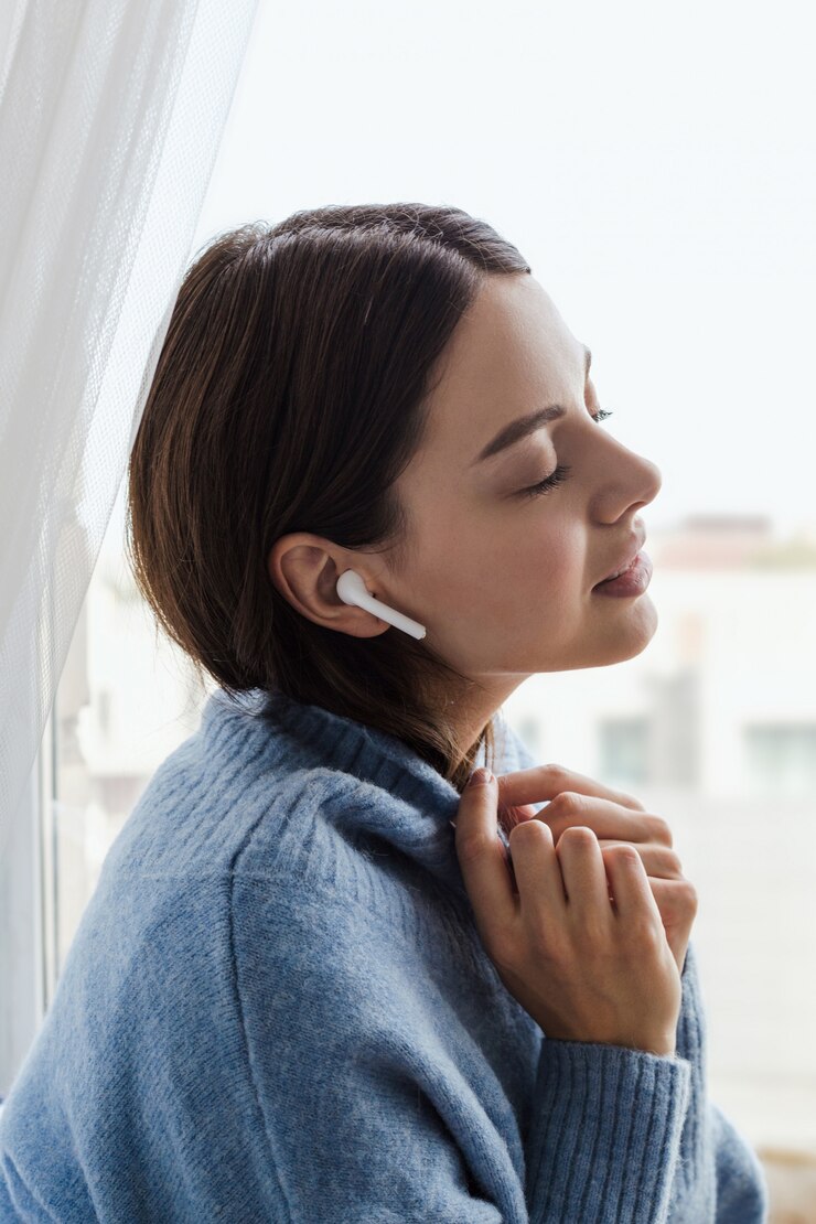 Menina com uma camisola azul perto da janela fones de ouvido escuta música