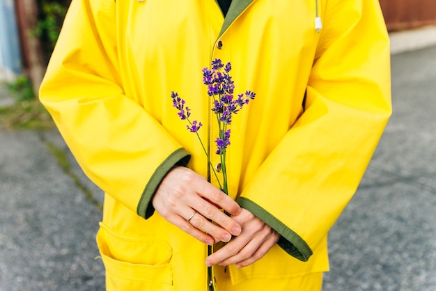 Menina com uma capa de chuva amarela segurando hastes de lavanda nas mãos