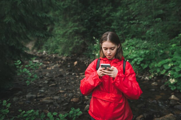 Menina com uma capa de chuva vermelha parada na floresta