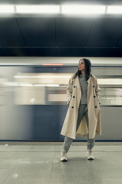 Foto menina com uma capa impermeável bege no metrô esperando o trem na plataforma